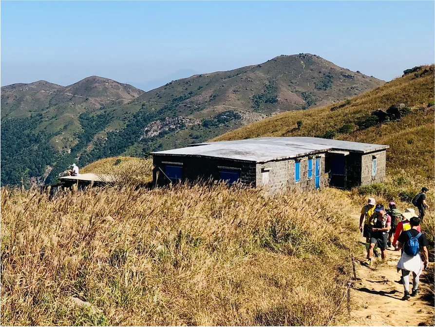 Hikers passing the Mess Hall at Lantau Mountain Camp Hikers walking past the stone Mess Hall at Lantau Mountain Camp in 2022